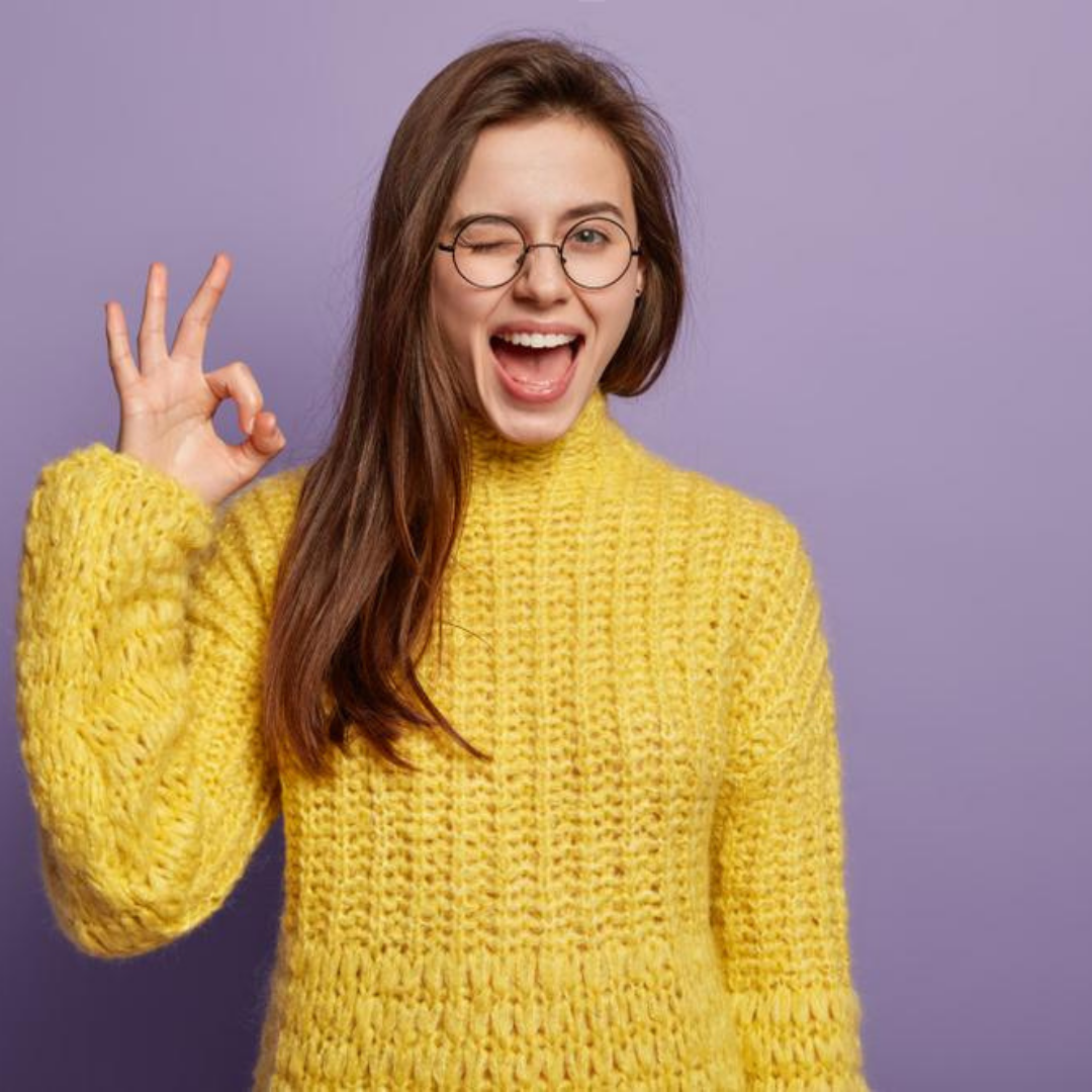 Young woman wearing glasses, winking and making the 'okay' symbol with her fingers